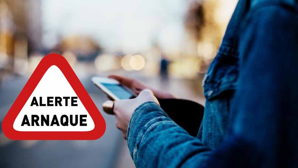 Panneau d'alerte rouge "ARNAQUE" devant une personne tenant un smartphone, symbolisant une arnaque bancaire par SMS.